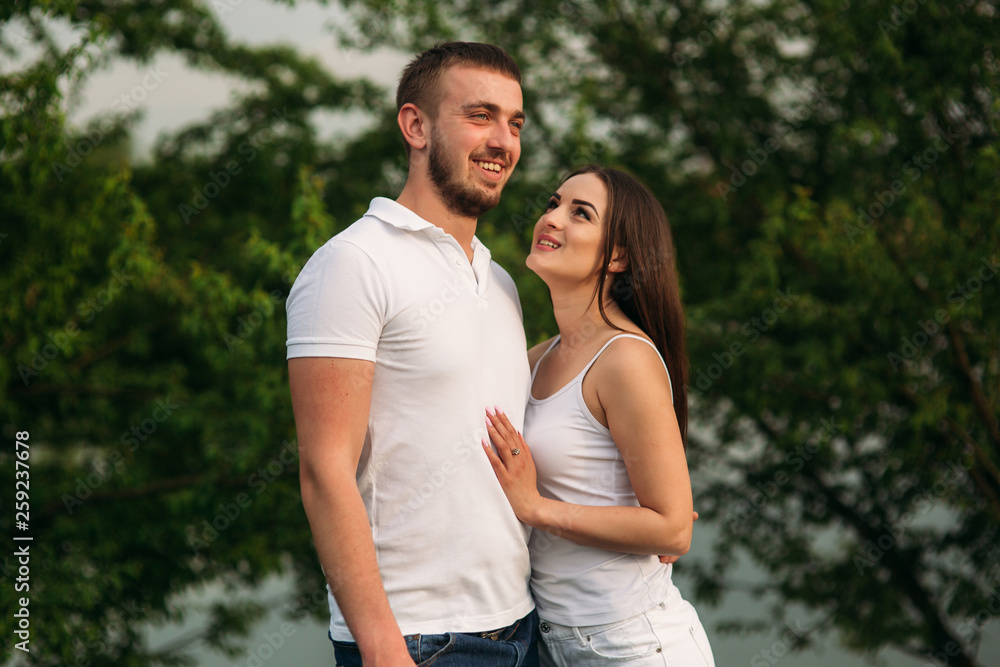 Obraz premium Young couple in white stand on the hill. Background of trees and lake