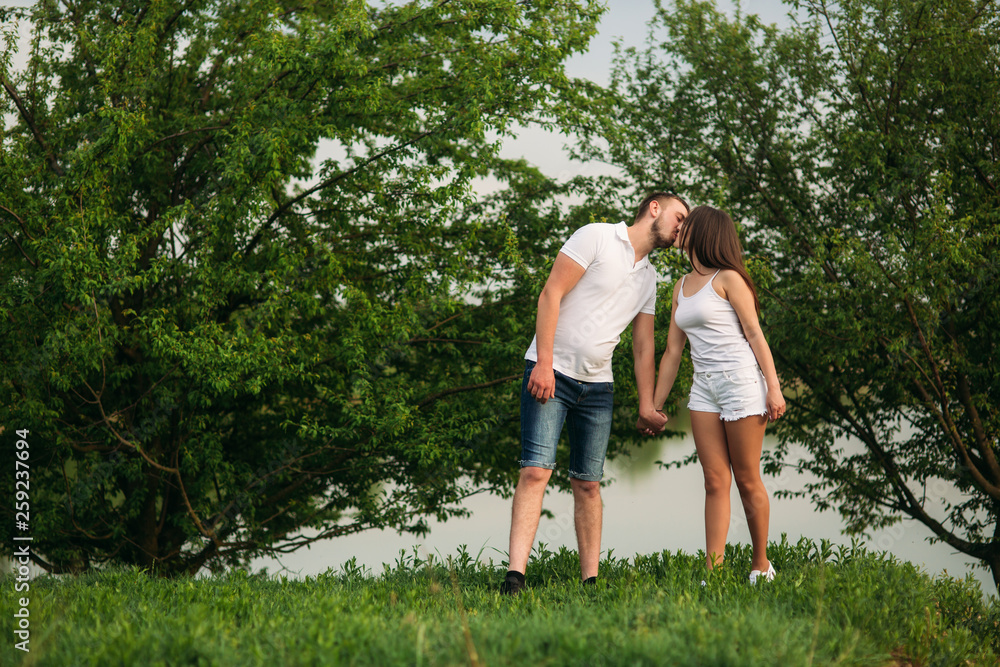 Young couple in white stand on the hill. Background of trees and lake Young couple in white stand on the hill. Background of trees and lake