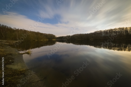 Cloudy night on the shore of the quiet lake in the forest