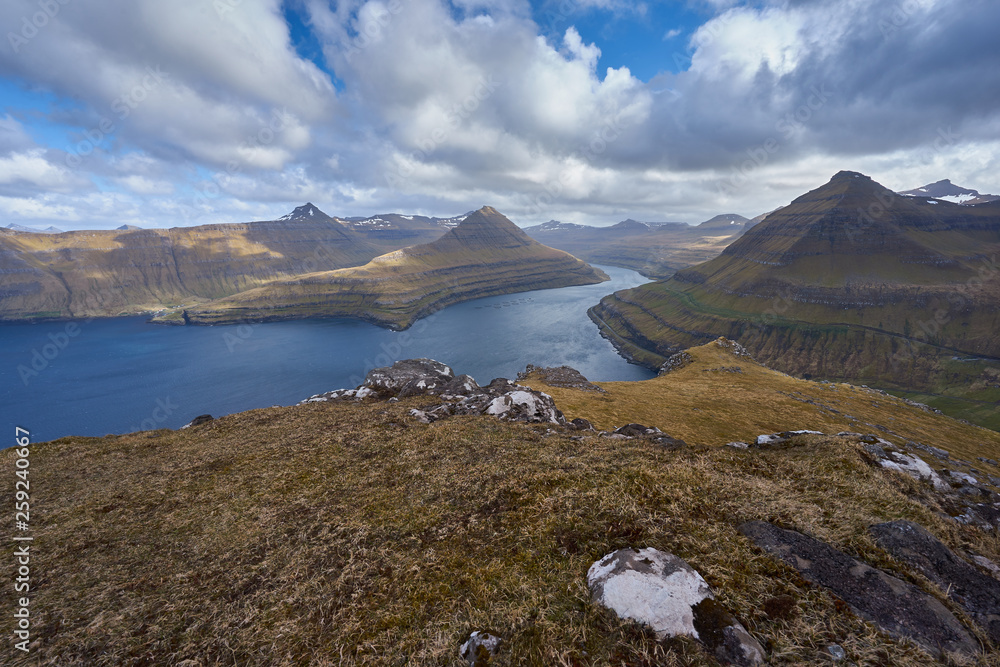 Scenic and epic landscape view from top of the one of thousand mountains in Faroe island into the deep fjord with other high cliffs and mountains in spring sunny day.