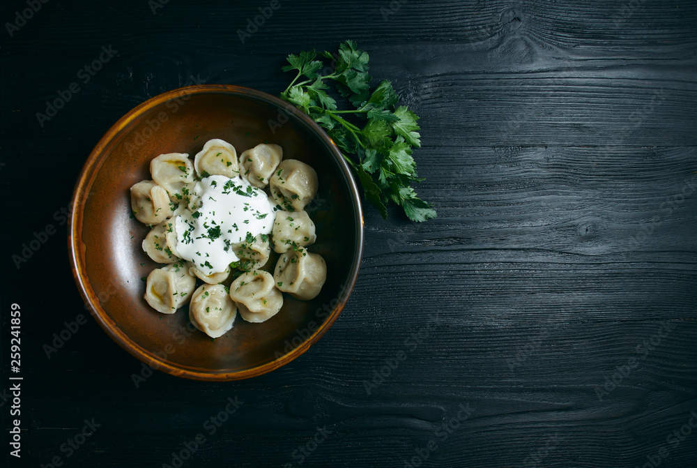 dumplings with sour cream and greens on a black wooden table. Russian traditional dish of dough and minced meat. close up photo. Copy space.
