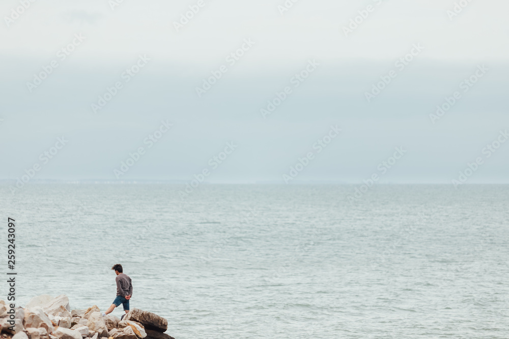 Young man standing on the rocks facing the sea on a cloudy day