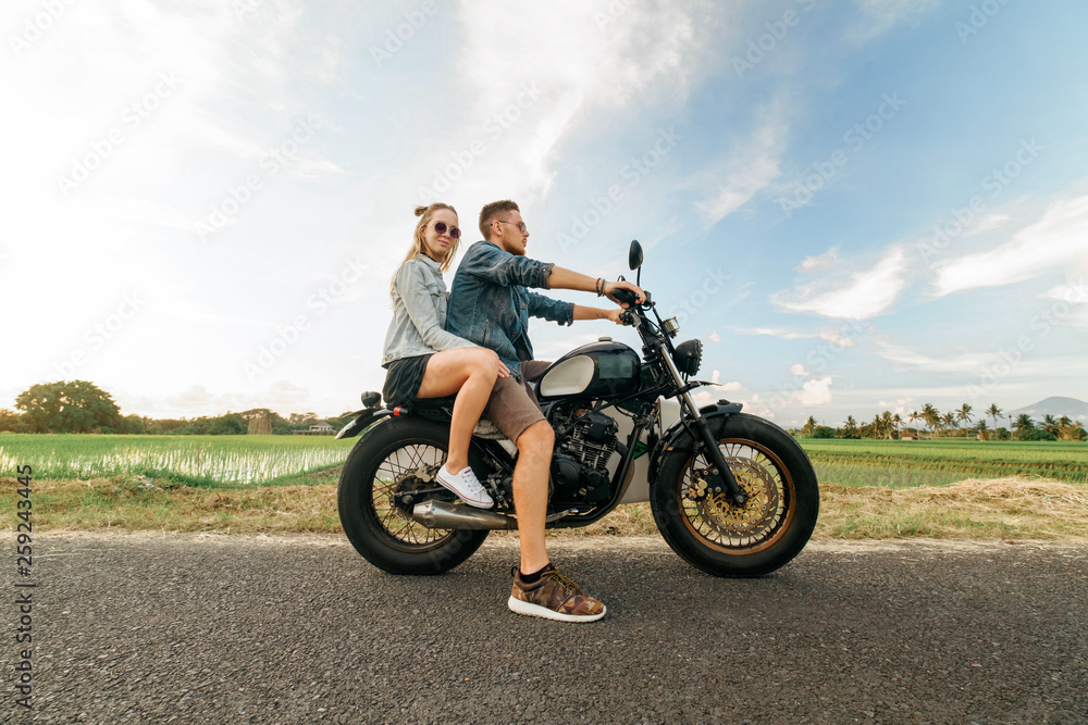 Trendy couple going by motorbike on tropical road Trendy couple going by motorbike on tropical road