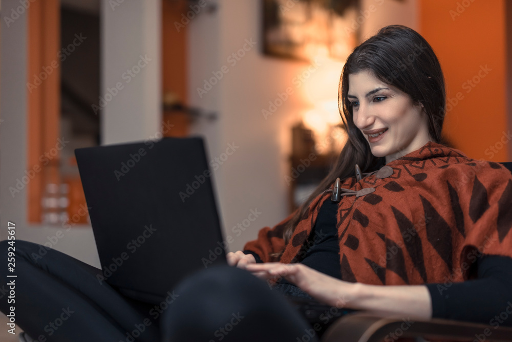 Beautiful woman sitting at home, using her computer to browse online content, enjoying her day off Beautiful woman sitting at home, using her computer to browse online content, enjoying her day off