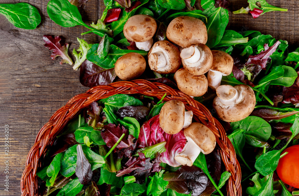 Basket with salad of fresh green leaves, tomato and mushroom champignon on a on rustic wooden table vegetable