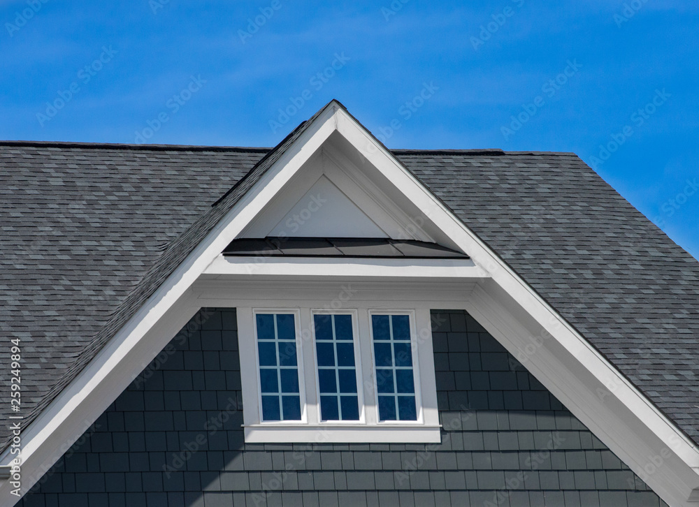 Attic three pane window on grey blue siding, gable, corbel, louver on a new construction luxury American single family home in the East Coast USA with blue sky background