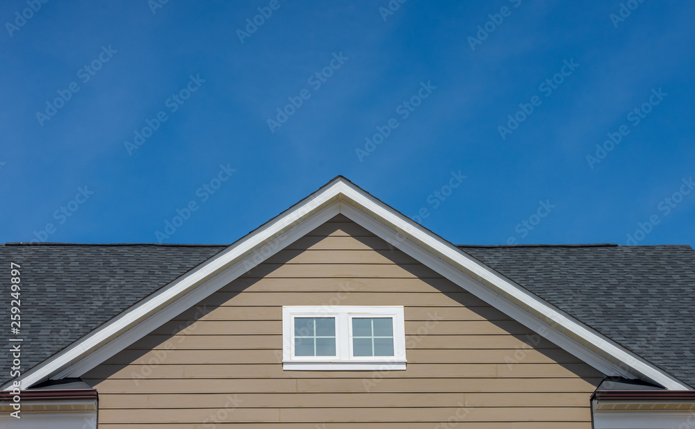 Attic window vent on brown siding, gable, corbel, louver on a new construction luxury American single family home in the East Coast USA with blue sky background fragment of the small wooden house, sky