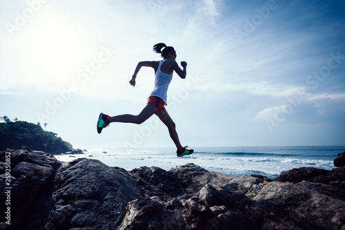 Young fitness woman trail runner running to rocky mountain top on seaside