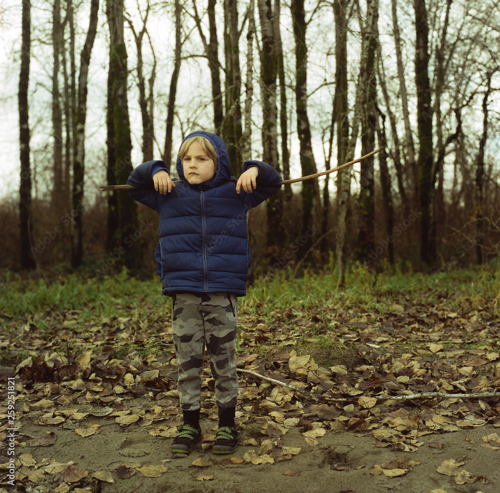 Boy stands with stick on his shoulders in front of a stand of trees in Portland, Oregon Boy stands with stick on his shoulders in front of a stand of trees in Portland, Oregon