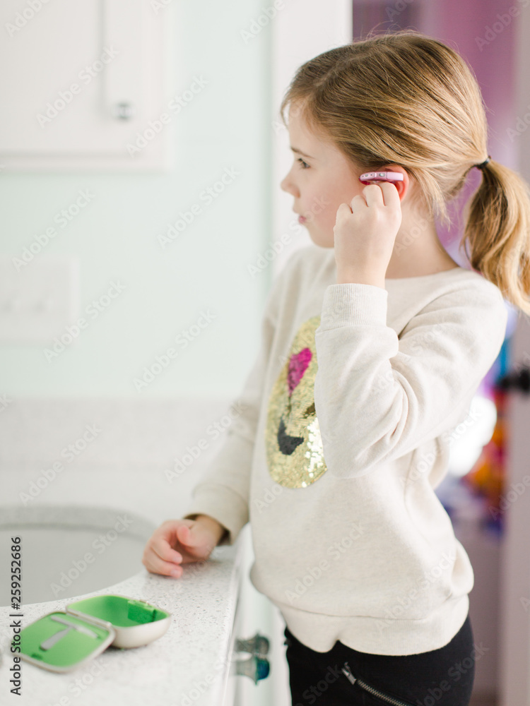 Young girl taking putting her hearing aids on Young girl taking putting her hearing aids on
