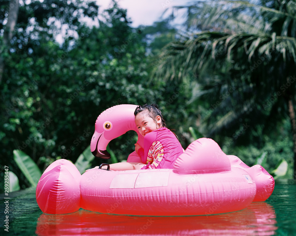Cute Asian girl playing in the pool with flamingo water toy. shot by ...