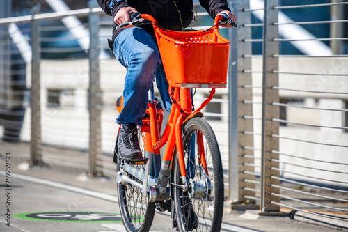 Man rides an orange bike with basket on bike path