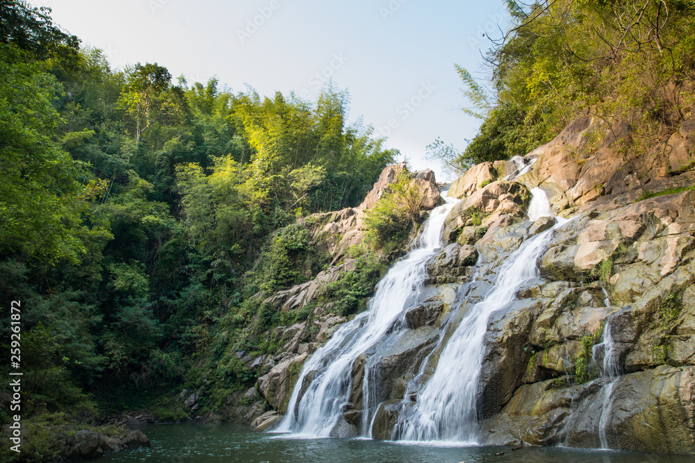 Beautiful large waterfall flowing between rocks in a deep green forest. Waterfall flowing over rocks. Nature background. Beautiful large waterfall flowing between rocks in a deep green forest. Waterfall flowing over rocks. Nature background.