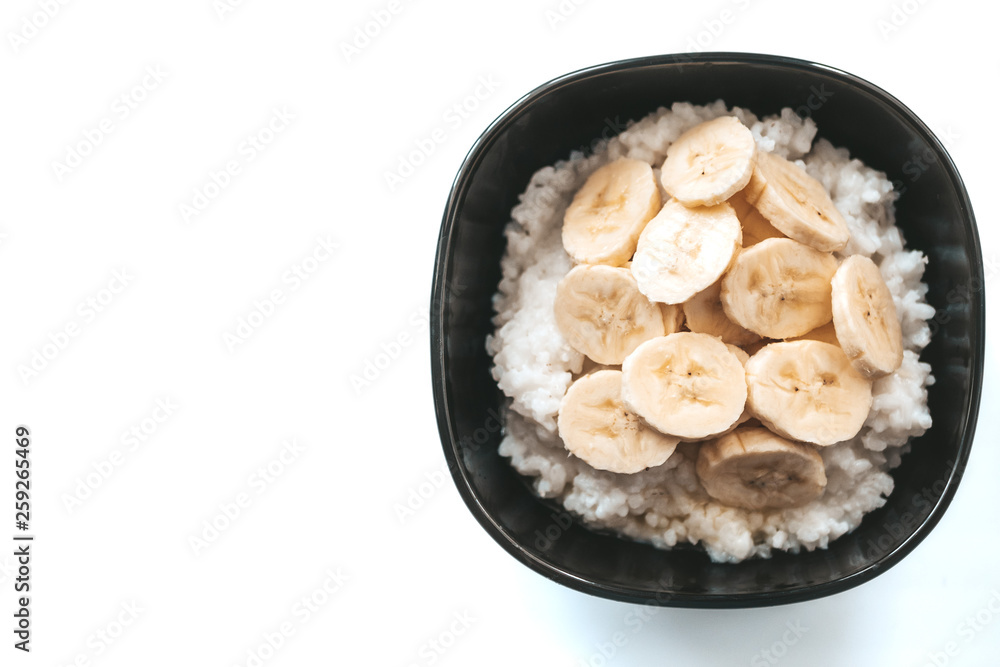 Rice milk porridge with banana in a black plate on a white background