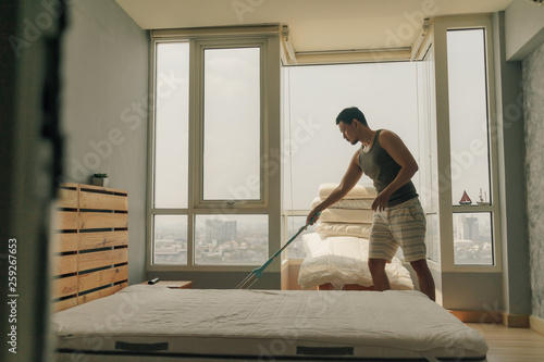 Asian man is cleaning his bedroom with warm summer light.