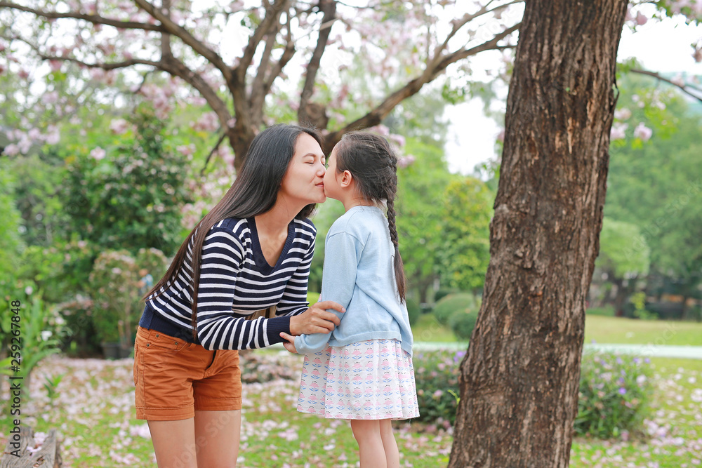 Happy mom kissing her daughter in garden with fully fall pink flower around outdoor. Happy mom kissing her daughter in garden with fully fall pink flower around outdoor.