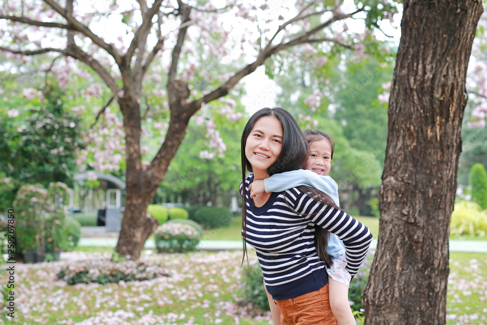 Smiling mom carrying her little child girl in garden with fully fall pink flower around. Happy loving family.