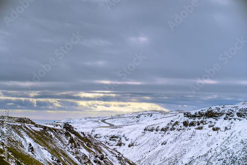Landscape photograph of snowy mountains with road in background and dramatic clouds