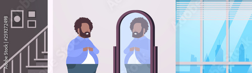 sad overweight man looking at himself reflection in mirror african american over size guy buttoning shirt unhealthy lifestyle obesity concept modern apartment interior flat portrait horizontal