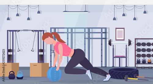 sporty woman doing crossfit exercises with medicine leather ball girl training cardio workout concept modern gym health studio club interior horizontal full length