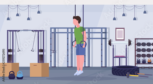 sporty man doing ring dips exercises with gymnastic rings guy training cardio crossfit workout concept modern gym health club studio interior horizontal full length