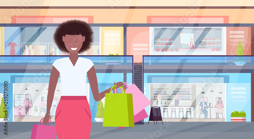 woman holding colorful shopping bags big sale concept african american girl walking modern retail mall with clothes and coffee shops supermarket interior horizontal portrait flat