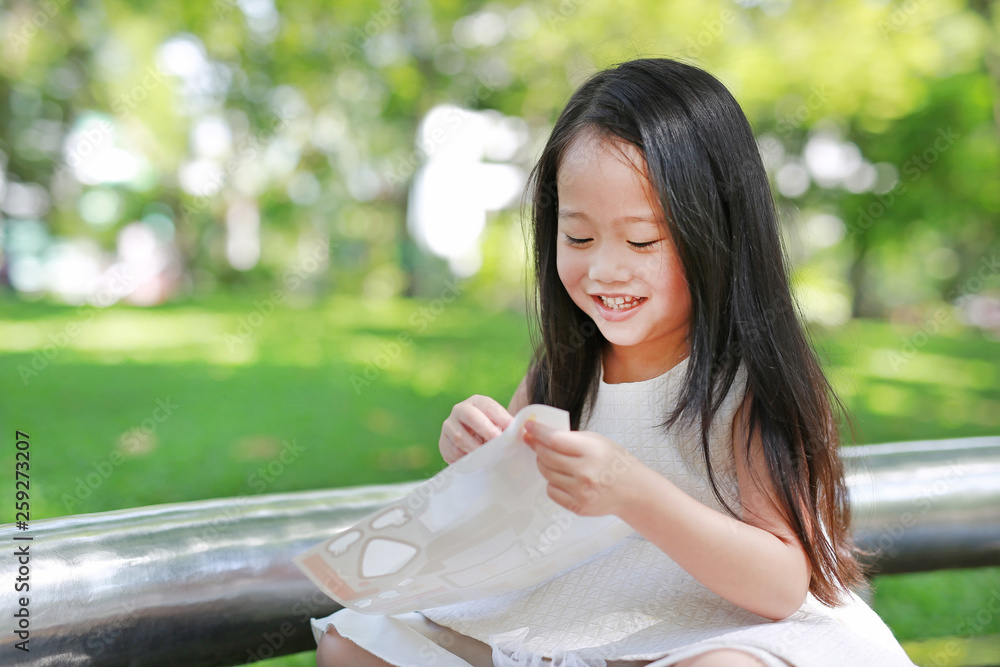 Happy little Asian child girl playing stickers in the green park. Happy little Asian child girl playing stickers in the green park.