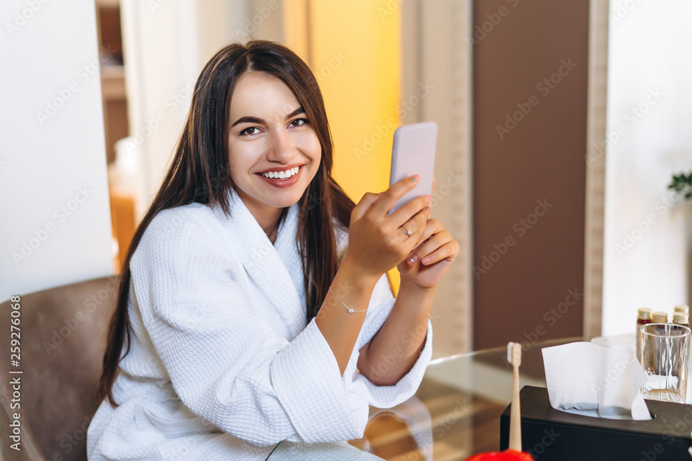 Young woman in bathrobe in hotel room using mobile phone Young woman in bathrobe in hotel room using mobile phone