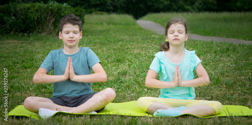 boy and girl doing yoga, outdoors, on a background of green grass, sitting on a gymnastic mat