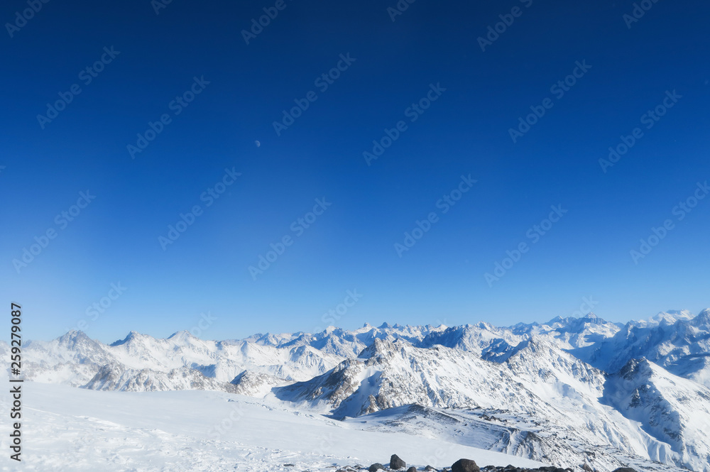 Moon above the snowy glacier of Caucasian Mountains in the blue sky. Elbrus region