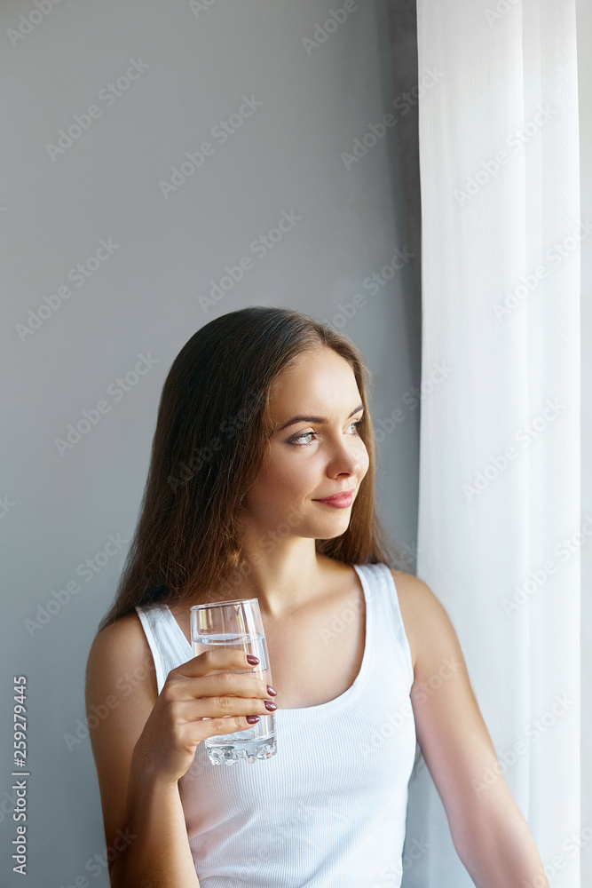 Healthy lifestyle. Young woman show glass of water. Girl drinks water. Portrait of happy smiling female model holding transparent glass of water. Health,Beauty, Diet concept Healthy lifestyle. Young woman show glass of water. Girl drinks water. Portrait of happy smiling female model holding transparent glass of water. Health,Beauty, Diet concept