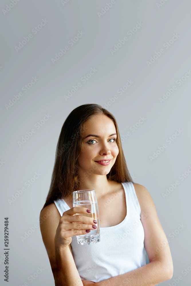 Healthy lifestyle. Young woman show glass of water. Girl drinks water. Portrait of happy smiling female model  holding transparent glass of water. Health,Beauty, Diet concept
