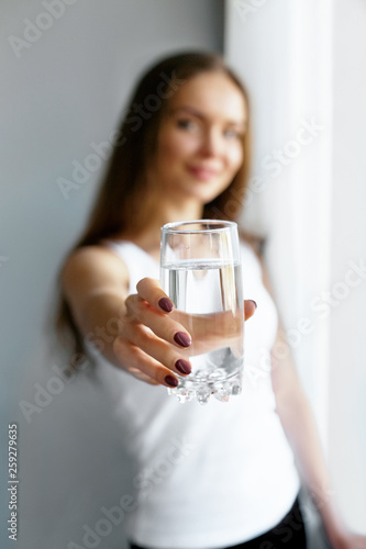 Closeup young woman show glass of water. Portrait of happy smiling female model holding transparent glass of water.Healthy lifestyle. Beauty, Diet concept