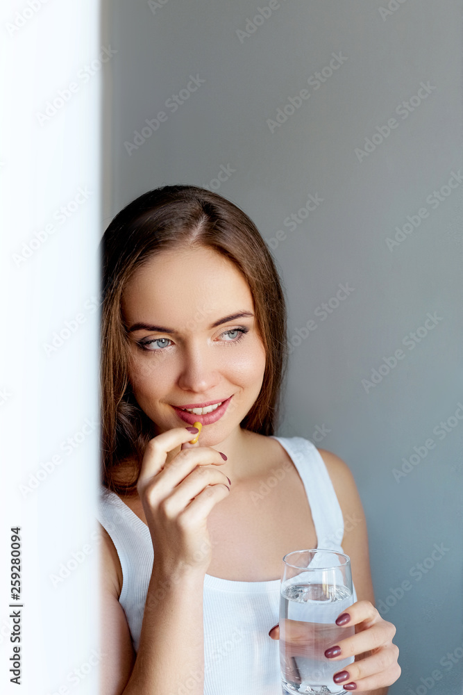 Happy smiling positive woman eating the pill and holding the glass of water in the hand, in her home. Happy smiling positive woman eating the pill and holding the glass of water in the hand, in her home.