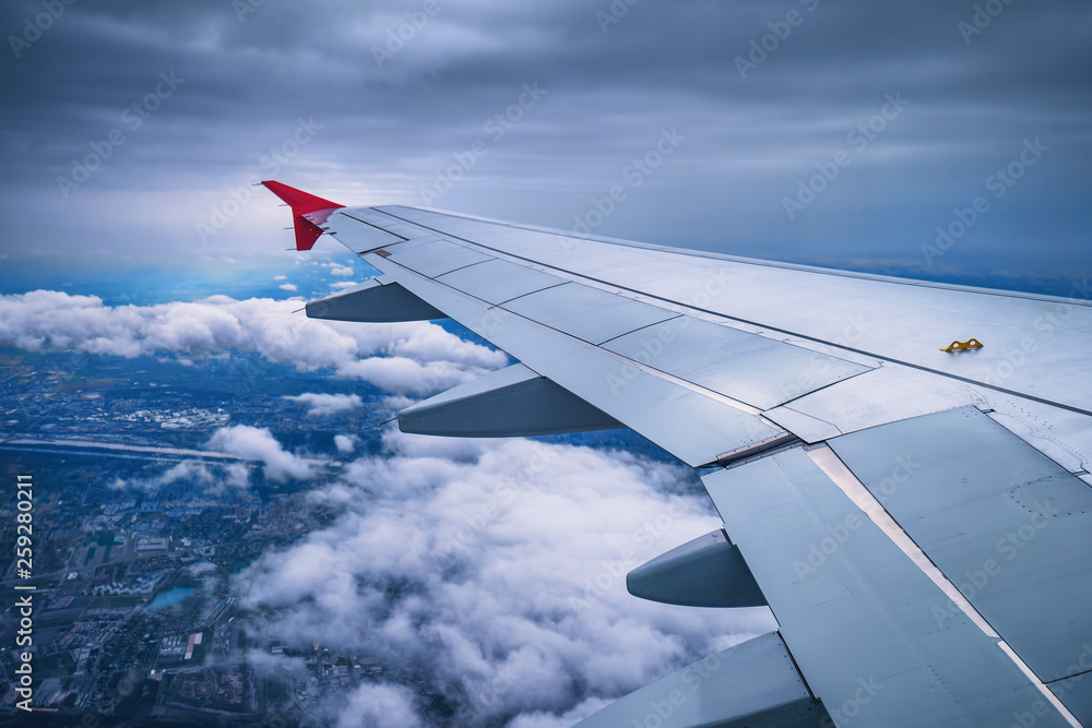 Wing of an airplane flying above the sky with clouds and city land