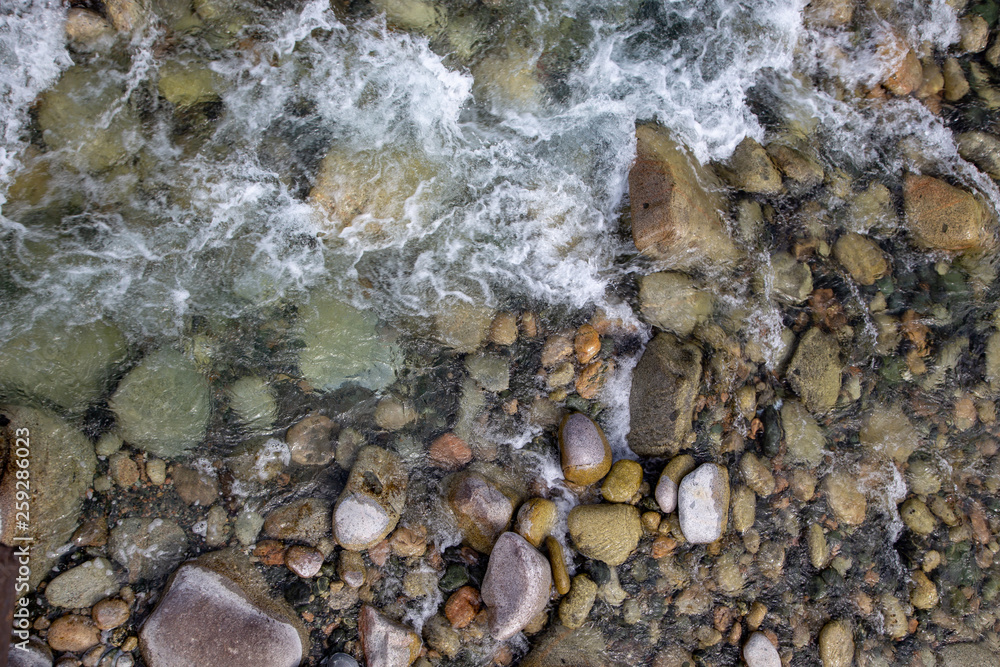 Water in the mountain raging river. Beautiful natural background of stones and water. Texture of clear water and fast river. Background to insert text. Tourism and travel. Water in the mountain raging river. Beautiful natural background of stones and water. Texture of clear water and fast river. Background to insert text. Tourism and travel.