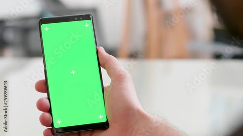 Close-up shot of a smartphone with green screen on in man's hand. Fuzzy background. Office style concept.