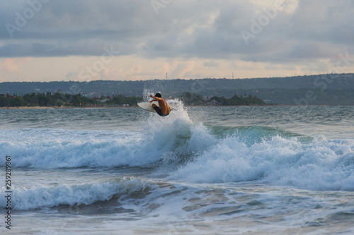Surfer with a tanned body performs a trick on a short board - a jump over the waves. 