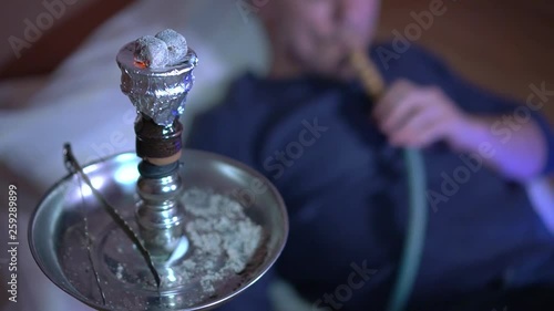 Close-up of a hookah bowl with burning coals. A young guy smokes a hookah, exhales smoke. Hookah smoke. On a plan, a young guy smokes a hookah. photo