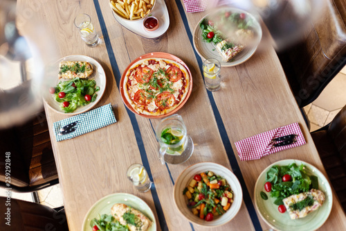 High angle view of main dishes, pizza, salad and homemade lemonade served on wooden dinner table for four