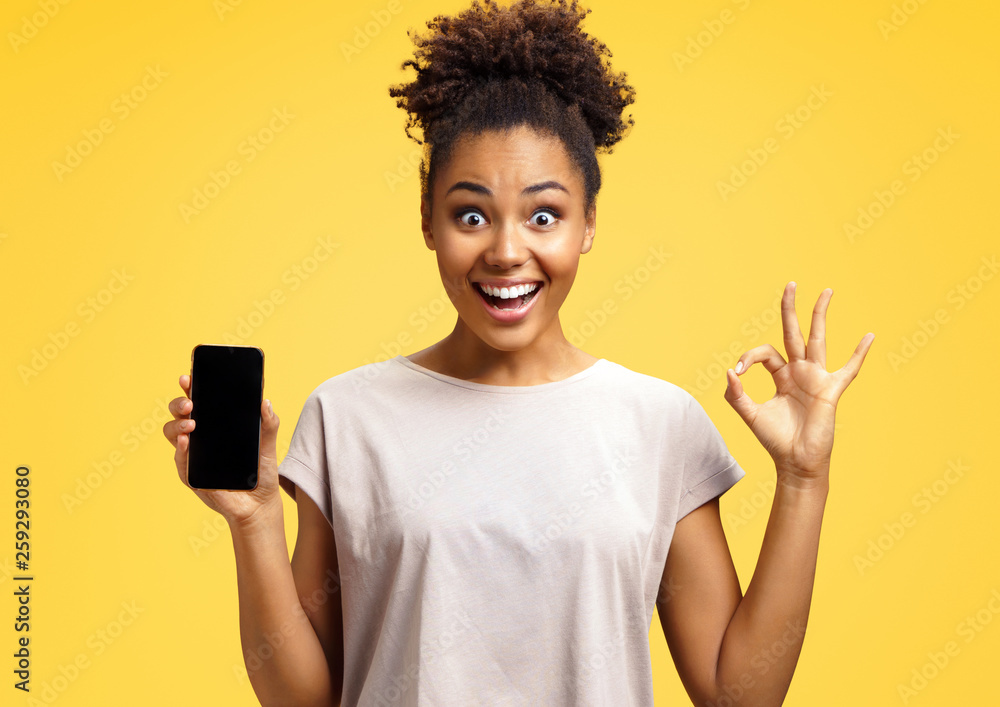 Overjoyed happy girl holds mobile phone and makes okay gesture. Photo ...