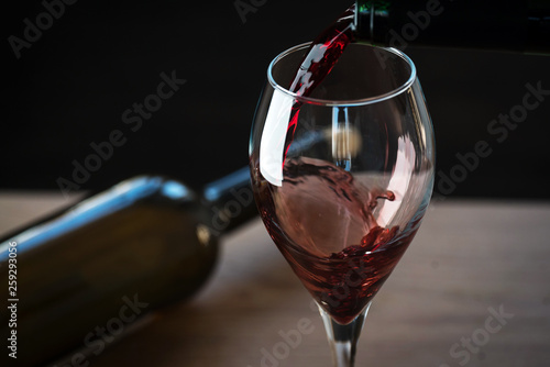 Pouring red wine into the glass against wooden background