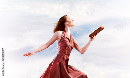 Girl against cloudy sky with opened book in palm as idea for knowledge