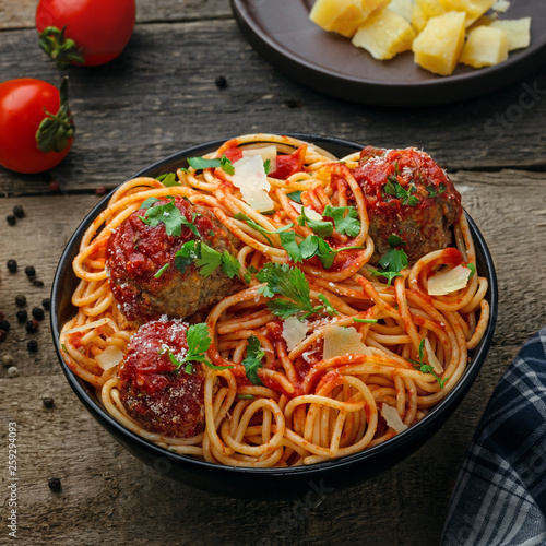 Delicious spaghetti pasta with meatballs and tomato sauce in a bowl. Traditional American Italian food on a rustic wooden table.