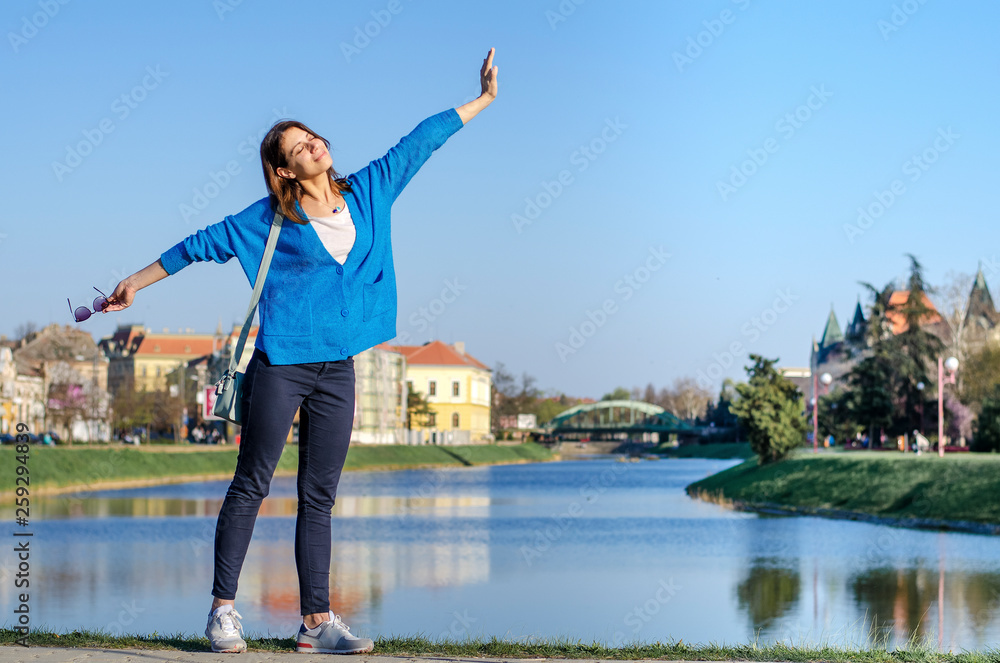 Girl celebrating spring time in the city by the lake, spreading her arms