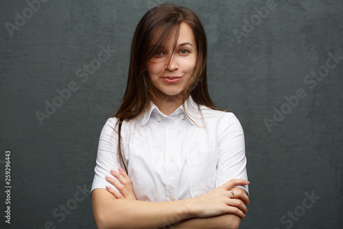 Portrait of pretty girl in strict casual clothes with tousled hair against the background of a gray wall.