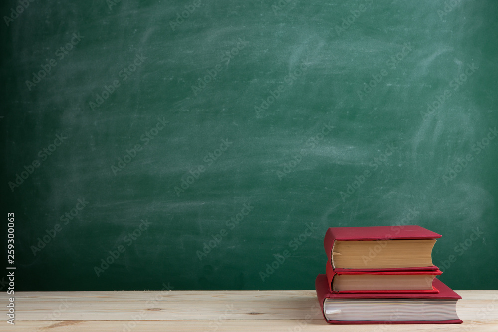 Education and reading concept - group of colorful books on the wooden table in the classroom, blackboard background Education and reading concept - group of colorful books on the wooden table in the classroom, blackboard background