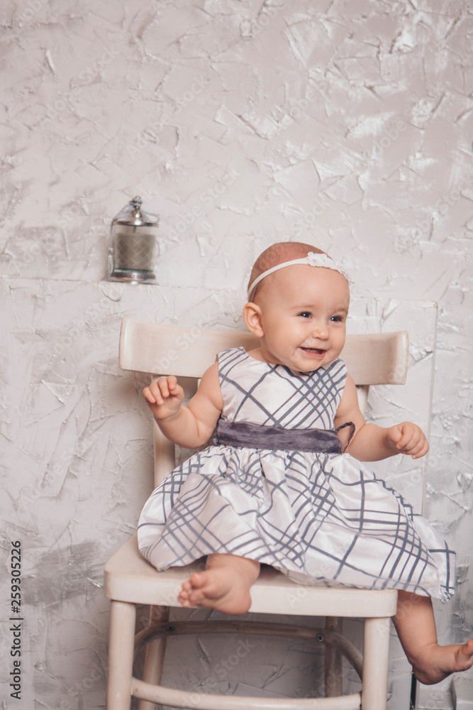 Naklejka premium a little girl in a dress sits on a chair and smiles
