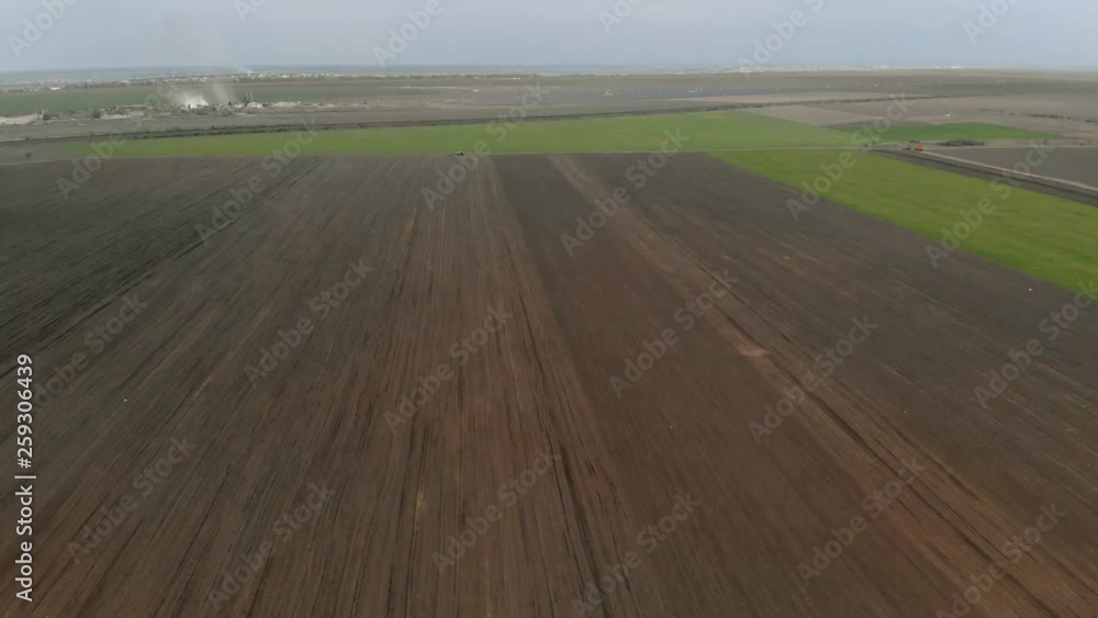 Aerial survey of treated field and agricultural machinery standing in distance on break from work. Copter shoots video landscape of farmland and growing natural healthy food Aerial survey of treated field and agricultural machinery standing in distance on break from work. Copter shoots video landscape of farmland and growing natural healthy food