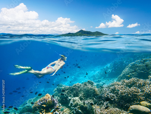 Woman swims around a coral reef surrounded by a multitude of fish on the background Islands..North Sulawesi, Indonesia.